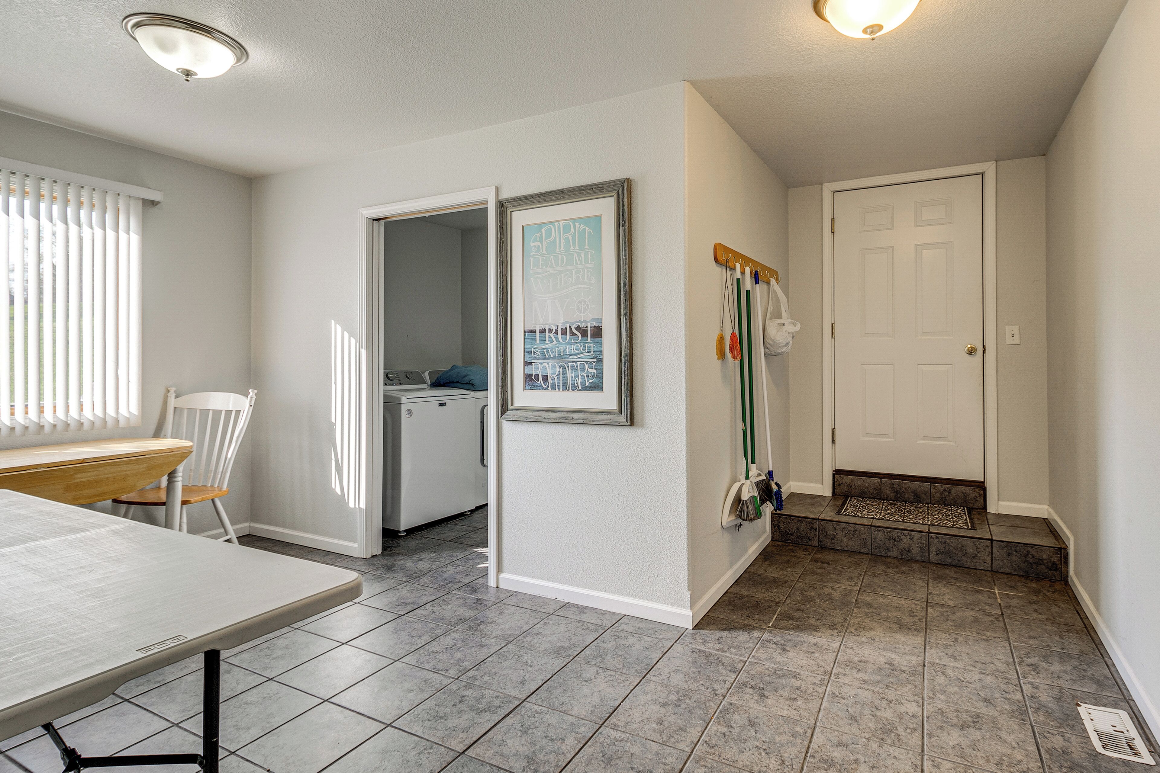 A clean, well-lit room with a dining table, a chair, a kitchen area, and a door with a coat rack.