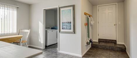 A clean, well-lit room with a dining table, a chair, a kitchen area, and a door with a coat rack.