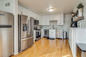 Una cocina moderna con electrodomésticos de acero inoxidable, armarios blancos y piso de madera.