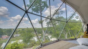 Quarto com uma janela grande que oferece vista para um lago e árvores, uma guitarra e um tapete felpudo branco.