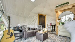 Interior de uma tenda com uma guitarra, um sofá, uma mesa de centro, cômoda e um espelho.