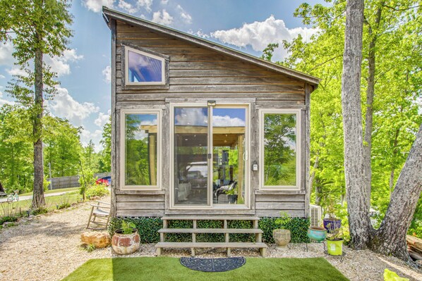 A wooden cabin with a large window, a bench, and potted plants.
