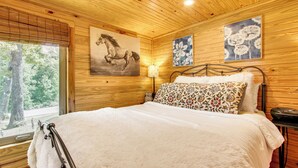 A wooden-paneled room with a bed, a window, and two wall-mounted paintings. - Tiny Cabin Getaway in the Tennessee River Valley (Rogersville)