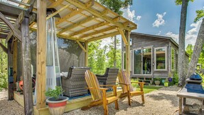 A wooden gazebo with two Adirondack chairs, a large planter, and a small building with windows. - Tiny Cabin Getaway in the Tennessee River Valley (Rogersville)