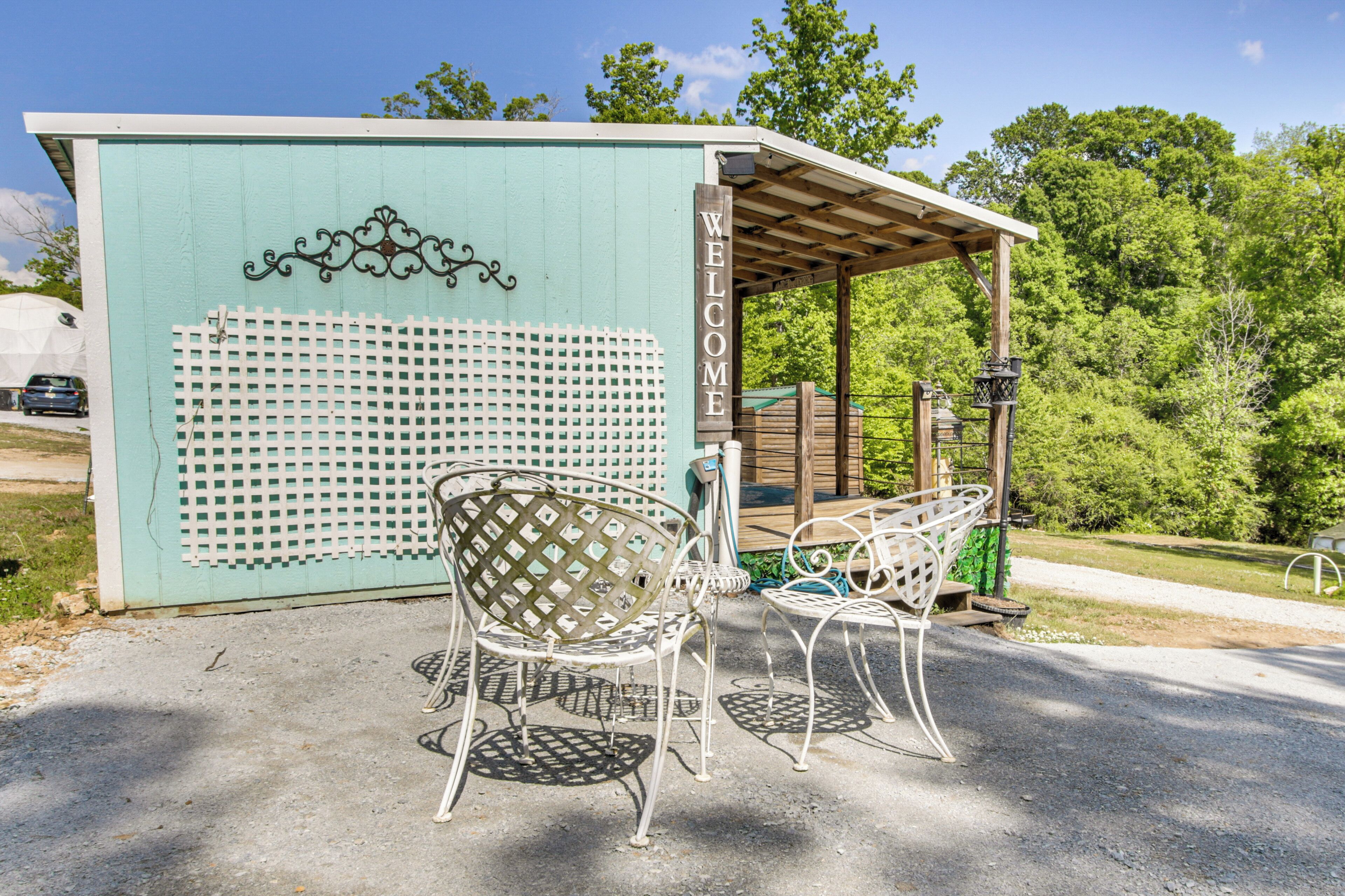 A gazebo with a 'WELCOME' sign, a lattice fence, and metal chairs.