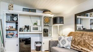 Eine kompakte Küche mit Mikrowelle, Kaffeemaschine und kleinem Kühlschrank. Ein Sofa mit gemusterten Kissen und ein großes Spiegelbild darüber.