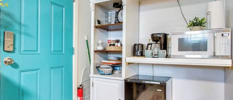 A teal door, a white cabinet with shelves, a microwave, and a small appliance.