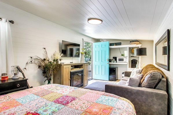 Un dormitorio con cama, escritorio, silla, armario, televisor, puerta y ventana.