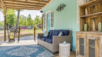 A covered porch with a wicker sofa, a small round table, and a decorative cabinet.