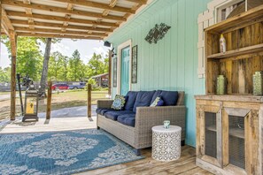 A covered porch with a wicker sofa, a small round table, and a decorative cabinet.
