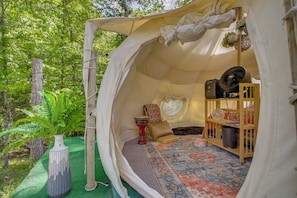 Une tente avec un tapis à motifs, un objet décoratif rouge et un ventilateur.