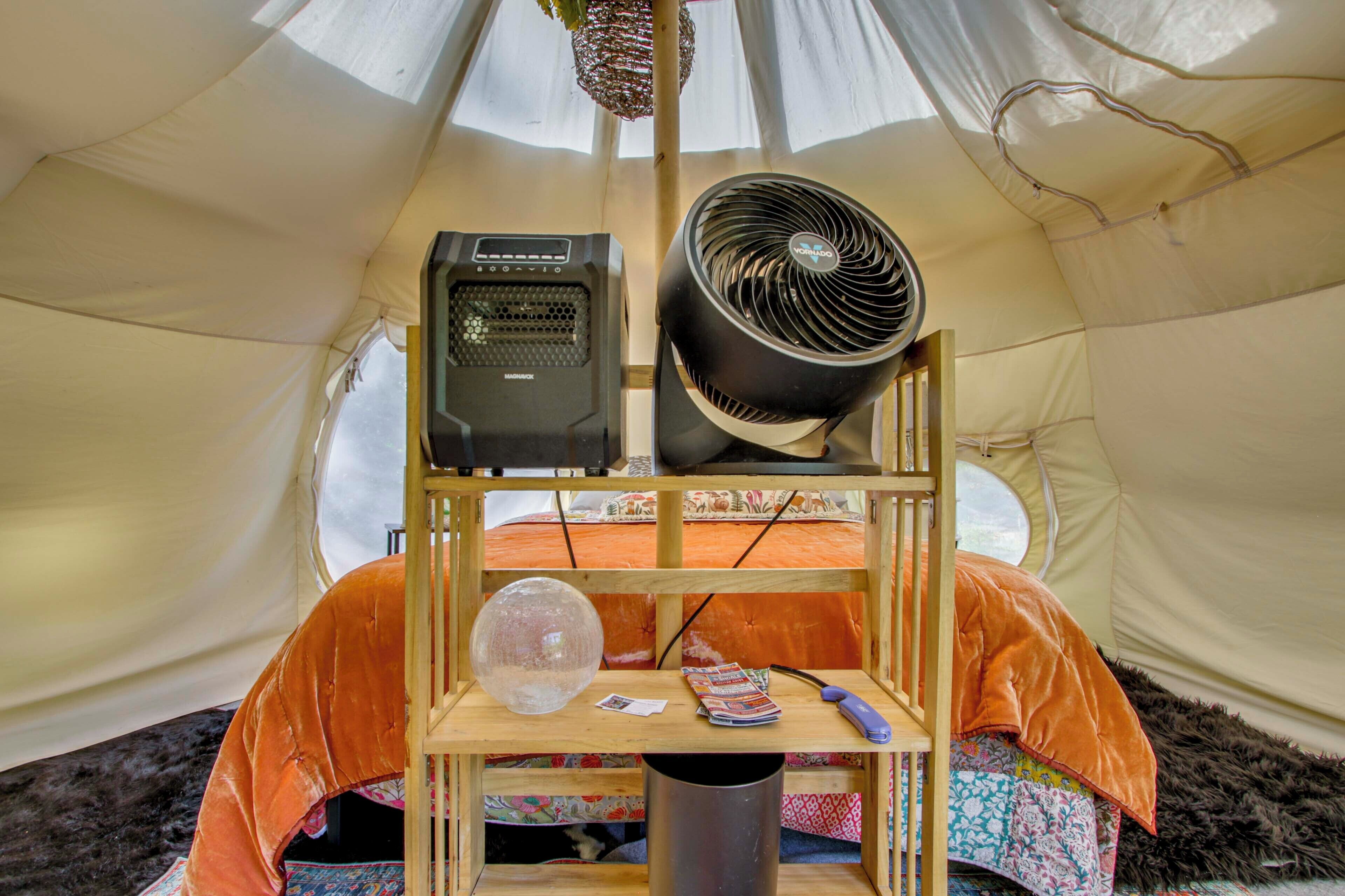 A tent interior with a bed, a fan, a heater, and a shelf with various items.