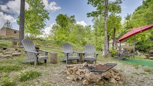 Ein Garten mit Adirondack-Stühlen, einer Feuerstelle und einem roten Sonnenschirm.