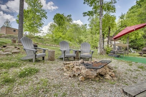 A backyard with Adirondack chairs, a fire pit, and a red umbrella.