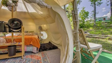 Una carpa con una cama, un ventilador, una mesa con una lámpara y una silla.