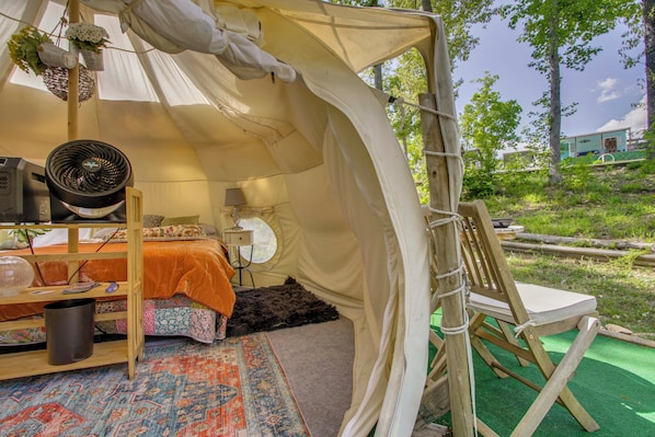 A tent with a bed, a fan, a table with a lamp, and a chair.