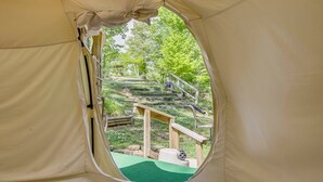 Ein Zelt mit Blick aus dem Fenster auf eine grüne, offene Landschaft mit Treppen und einer Holzkonstruktion.