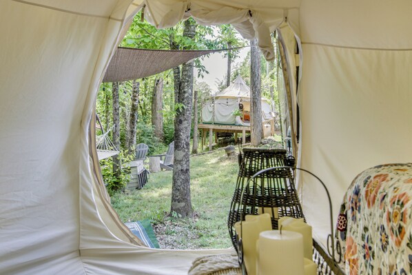 A tent with a view of a tree-lined area, a hammock, and a table with candles.