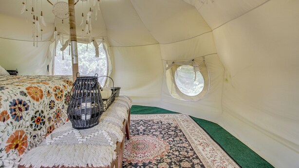 A tent with a bed, a woven basket, a patterned rug, and a circular window. - Unique Glamping Tent in Tennessee River Valley (Rogersville)