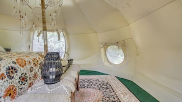 Una carpa con una cama, una cesta tejida, un tapete estampado y un ventanal circular.