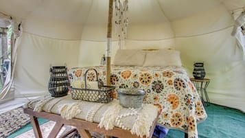A tent with a bed, a bench, a hanging light, and a small table with a basket and candle.