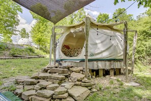 A rustic outdoor bed with a canopy, surrounded by rocks and greenery.