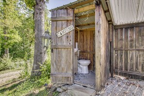 A rustic wooden structure with a toilet and a sign indicating 'CAMPING.'