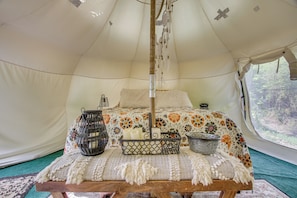 A tent with a bed, a hanging light, and a basket with candles.