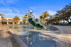 Un parco acquatico con uno scivolo verde, palme e un edificio sullo sfondo.