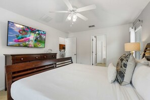 Ein Schlafzimmer mit einem Bett, einem Deckenventilator, einem Fernseher und einer Tür zu einem Badezimmer.