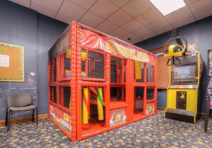 Uma área de recreação com uma estrutura de playground em formato de ônibus escolar, uma única cadeira e uma máquina de peguinhas.