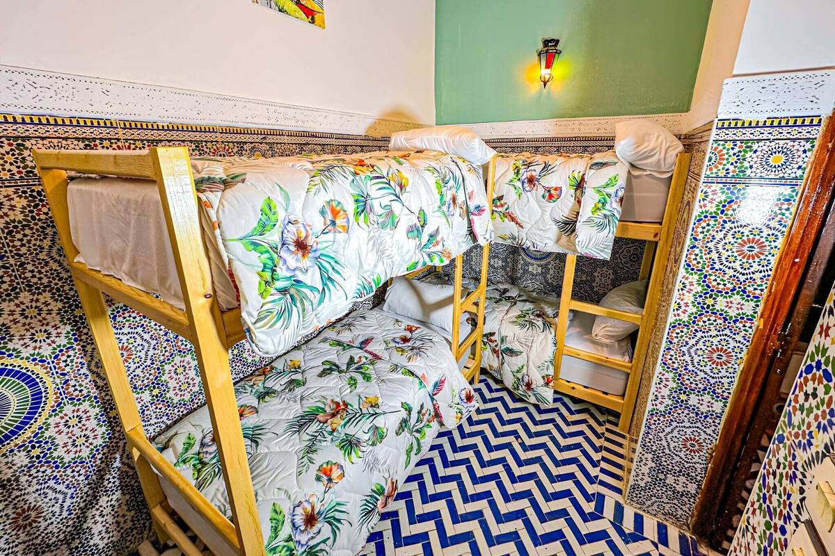 A bunk bed with floral bedding, a green wall, and patterned floor tiles.