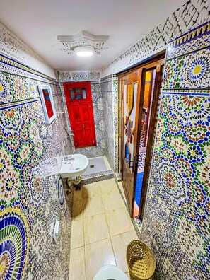 A bathroom with a red door, a white sink, and patterned walls. - Dar Lala Ghita (Fes)