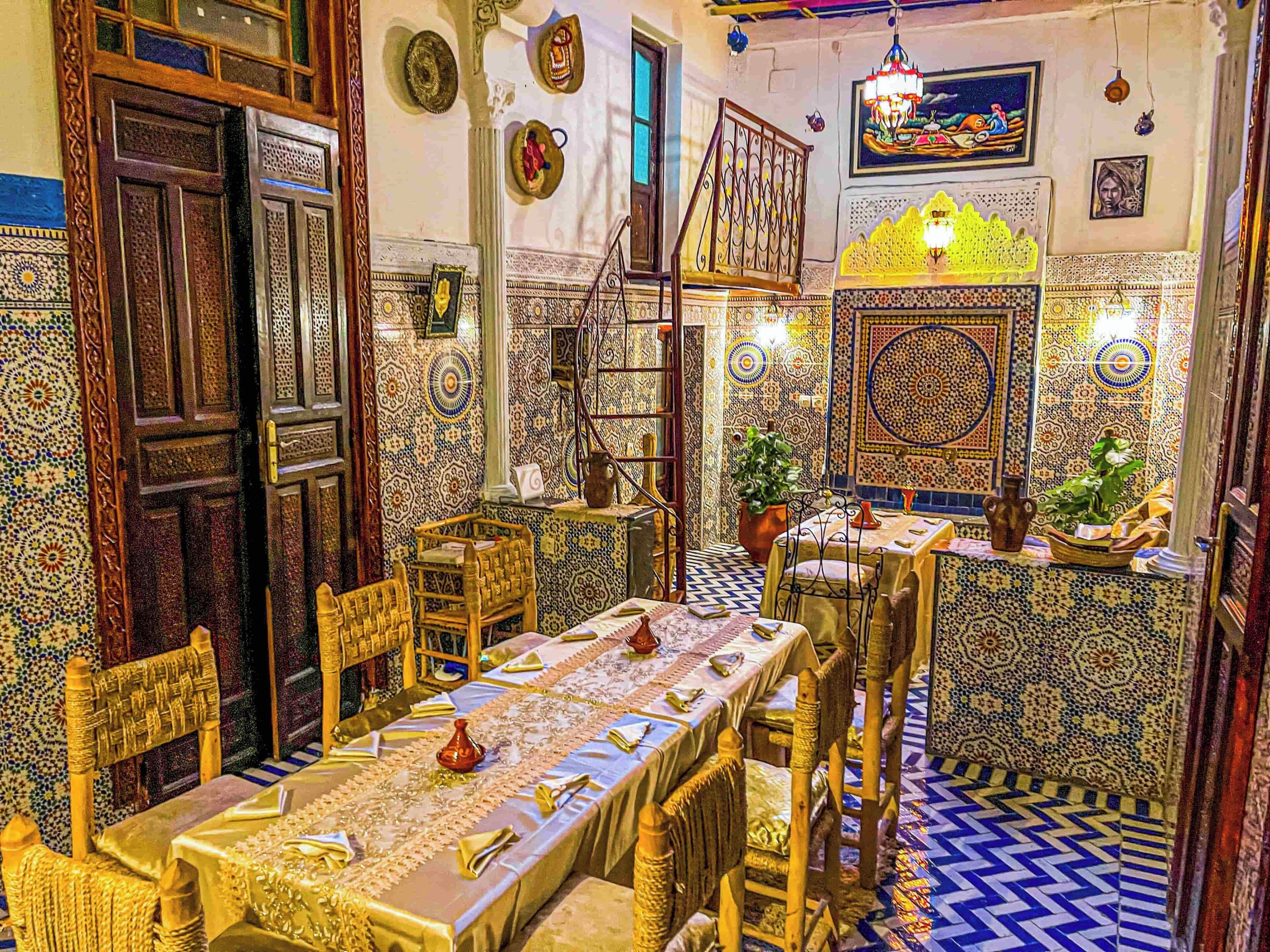 A traditional Moroccan interior with a long dining table, ornate chairs, and intricate tile work.
