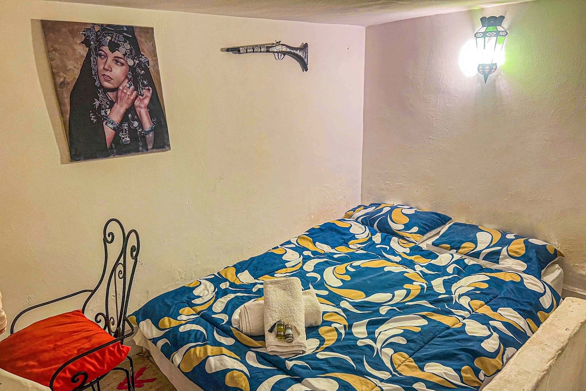A bedroom with a bed, a chair, a wall-mounted lamp, and a framed picture.