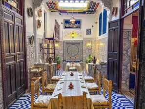 A traditional Moroccan interior with a long dining table, ornate doors, and intricate tile work. - Dar Lala Ghita (Fes)