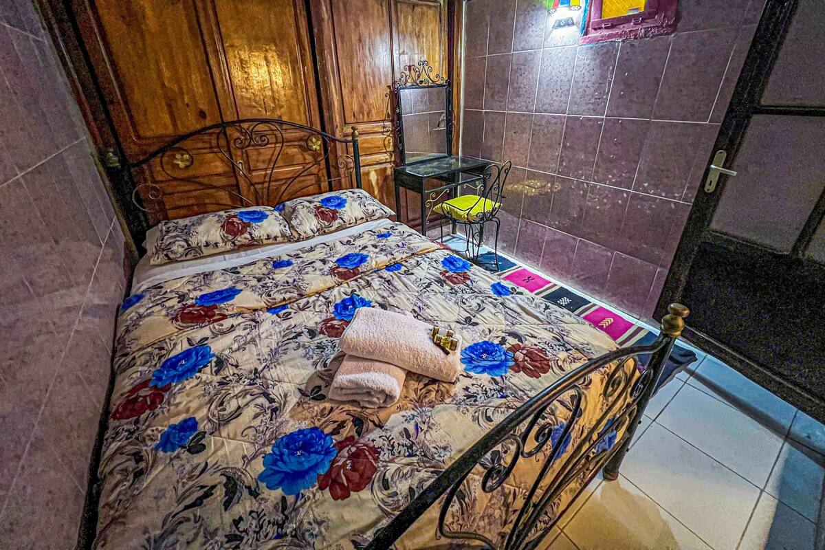 A bedroom with a bed, a chair, a small table, and a mirror.