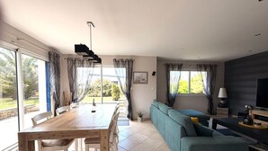 A modern living room with a dining table, sofa, and TV. - COMFORTABLE VILLA 5 MINUTES WALK FROM GRÈVE BLANCHE BEACH (Plouguerneau)