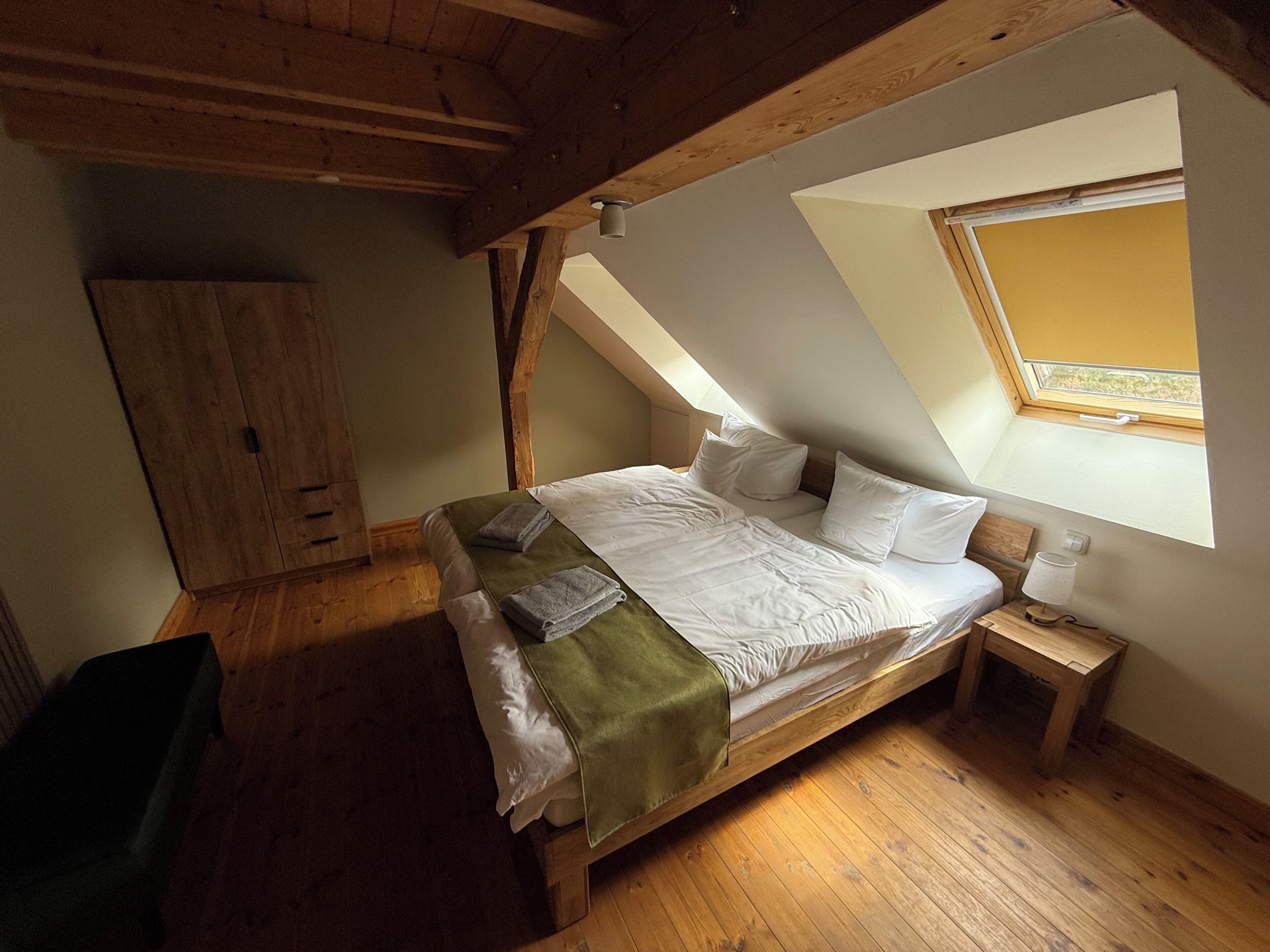 Ein Schlafzimmer mit schrägem Dach, einem Bett, einem Nachttisch, einem Kleiderschrank und einem Fenster.