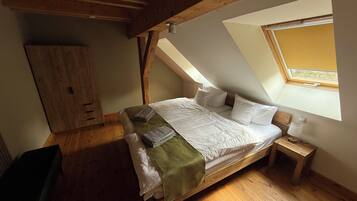 Ein Schlafzimmer mit schrägem Dach, einem Bett, einem Nachttisch, einem Kleiderschrank und einem Fenster.