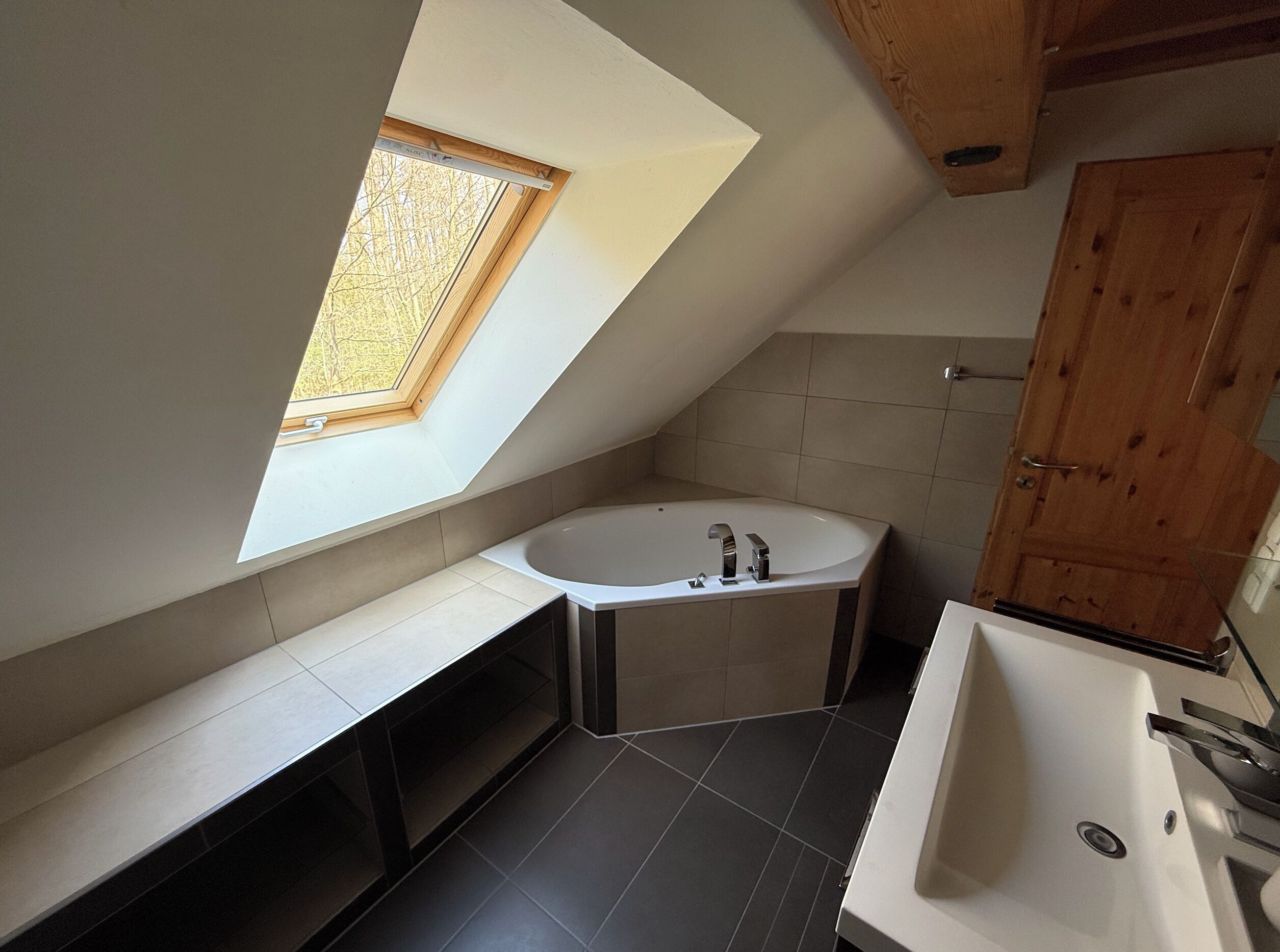 Ein modernes Badezimmer mit Oberlicht, Badewanne, Waschbecken und Holzschränken.