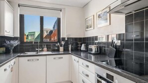 A modern kitchen with white cabinets, a black countertop, and a window with a view of buildings. - Windsor Castle Views - Spacious Flat - By Tempstay (Windsor)