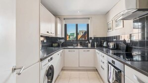 A compact kitchen with a washing machine, a sink, and a stove. - Windsor Castle Views - Spacious Flat - By Tempstay (Windsor)
