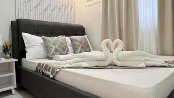 Una cama bien tendida con cabecera negra, ropa de cama blanca y almohadones decorativos.