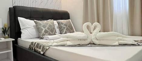 Ein ordentlich bezogenes Bett mit schwarzem Kopfteil, weißer Bettwäsche und dekorativen Kissen.