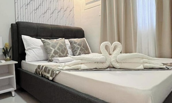Una cama bien tendida con cabecera negra, ropa de cama blanca y almohadones decorativos.