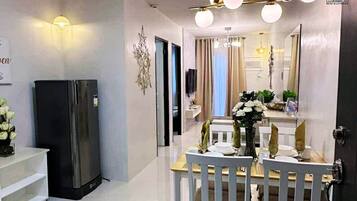 Una cocina moderna con un refrigerador negro, un comedor con una mesa y sillas blancas, y una araña.