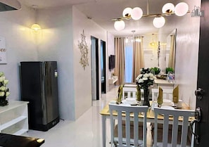 Una cocina moderna con un refrigerador negro, un comedor con una mesa y sillas blancas, y una araña.