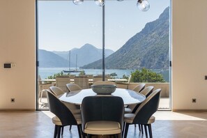 Zona pranzo con un grande tavolo e sedie, vista su un lago con barche e montagne sullo sfondo.