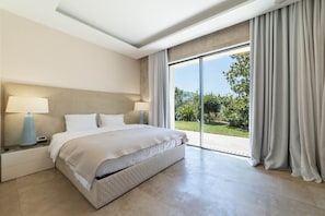 Una camera d'albergo con un letto, due comodini con lampade, una grande finestra con tende e vista sul verde.